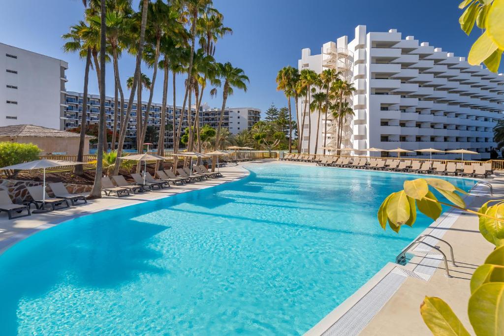 une grande piscine avec des chaises et des palmiers dans l'établissement Barceló Margaritas, à Playa del Ingles