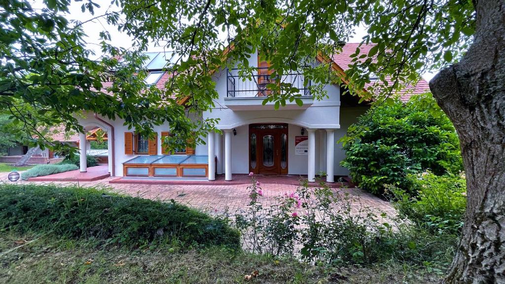 a white house with a red door and a tree at Őzkút Apartmanház in Ólmod