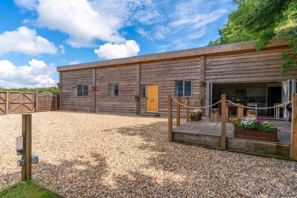 un gran edificio de madera con un patio delante de él en Old Stables, Little Ballthorns Farm en Cold Ashton