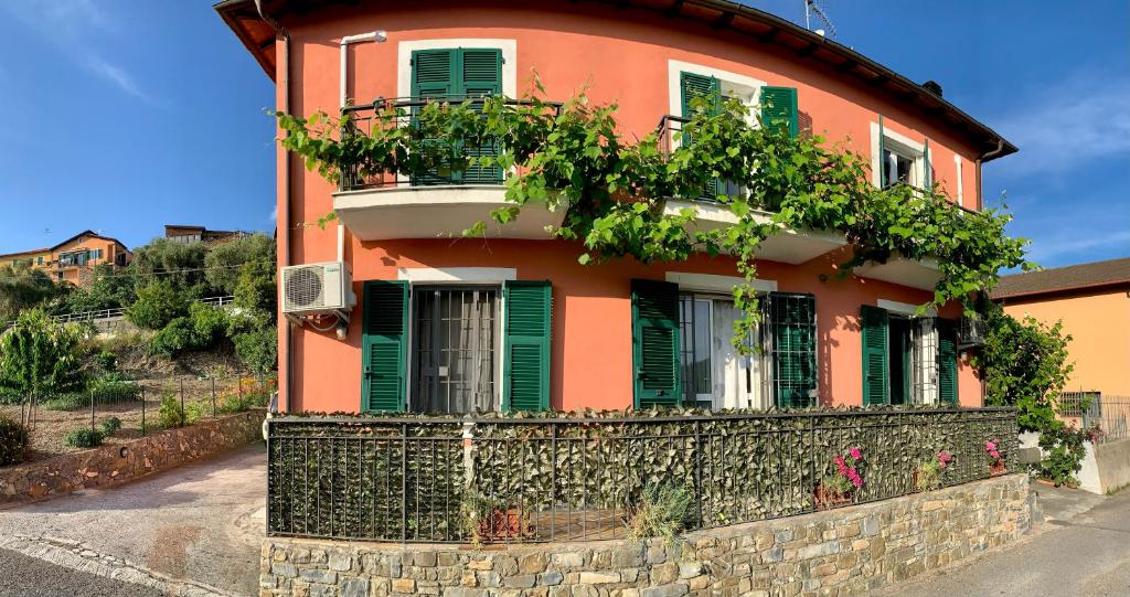 an orange house with green shutters and a stone wall at Ligo in Villanova dʼAlbenga