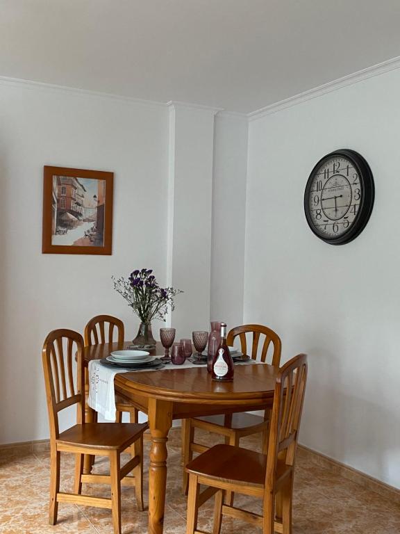 mesa de comedor con sillas y reloj en la pared en Apartamento Conde, en Corcubión