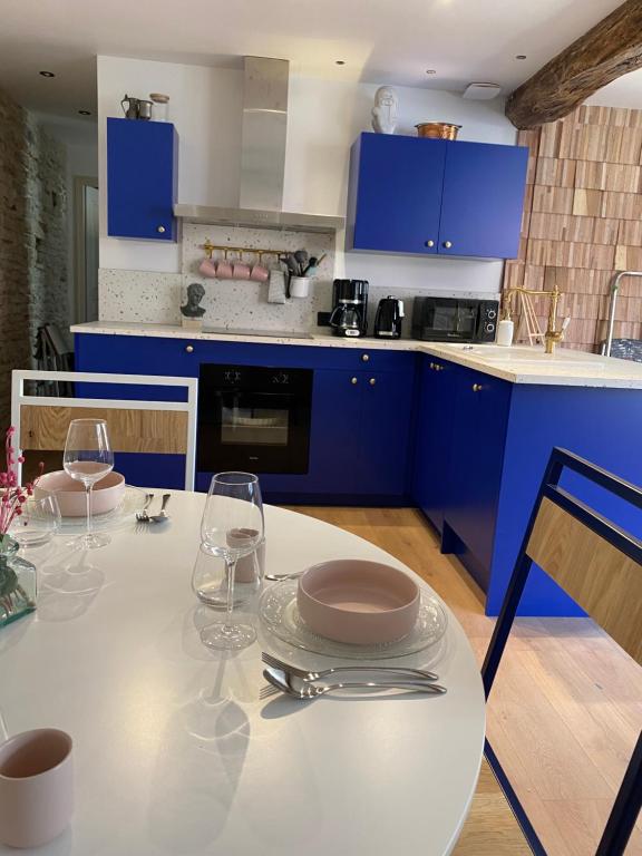 kuchnia z niebieskimi szafkami i białym stołem z kieliszkami do wina w obiekcie Logement entier - L'Appart des anges 1 w mieście Noyers-sur-Serein