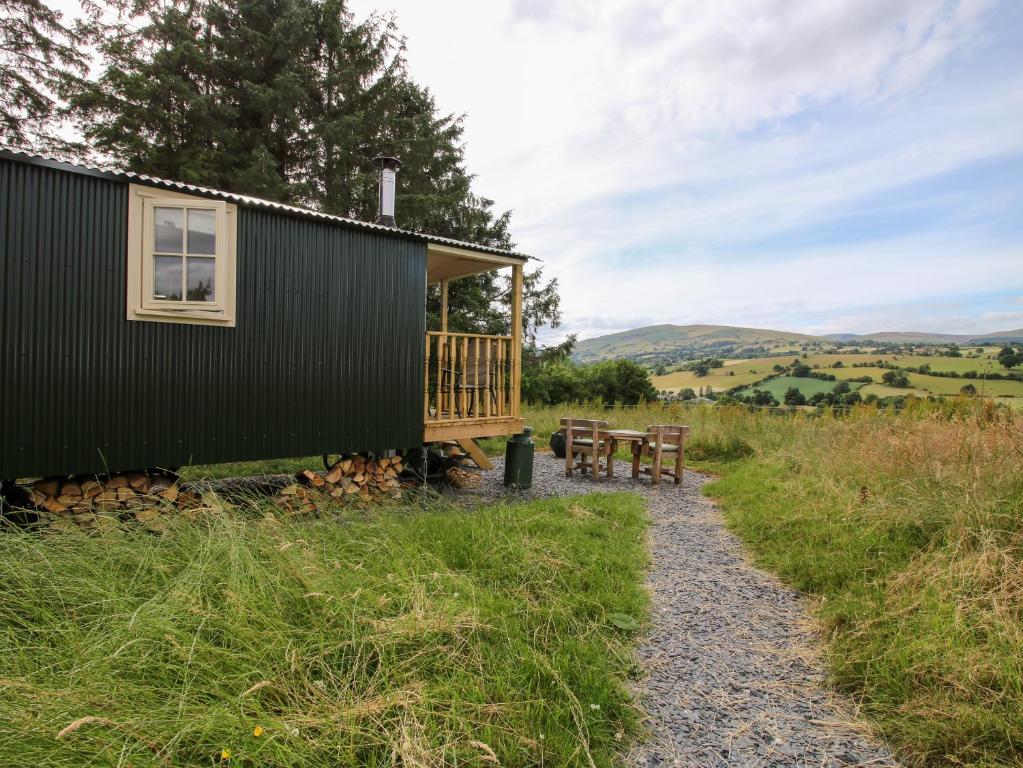 a green cabin with a table and two benches at Shepherd's Hut at Retreat in Llanrhaeadr-ym-Mochnant