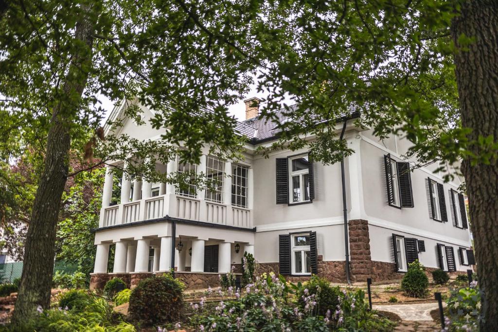 une maison blanche avec des volets noirs et des arbres dans l'établissement Villa Chez les Amis - Adults only, à Balatonszepezd