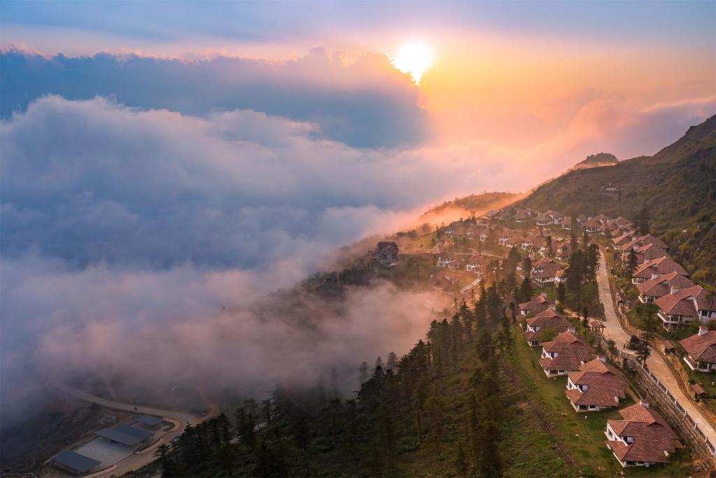 una vista aérea de un pueblo en las montañas con la puesta de sol en Ville De Mont Mountain Resort, en Sa Pa