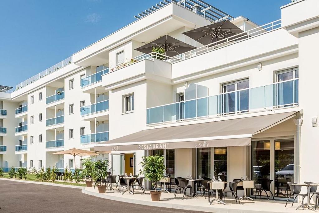 un immeuble d'appartements avec des tables et des chaises devant lui dans l'établissement Résidence Sénior Villa Sully Seynod-Annecy, à Annecy