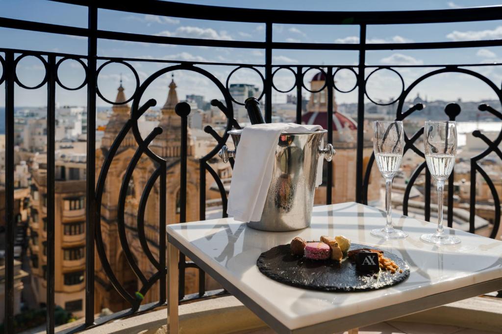 a plate of food on a table on a balcony with wine glasses at AX The Palace in Sliema