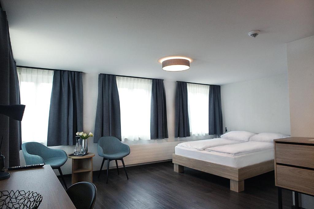 a bedroom with a bed and two chairs and windows at Dihei - Hotel, Lounge, Bar in Dübendorf