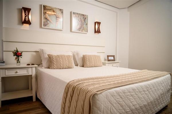 Pousada Ondas da Brava في إيتاجاي: غرفة نوم بيضاء مع سرير كبير وطاولتين
