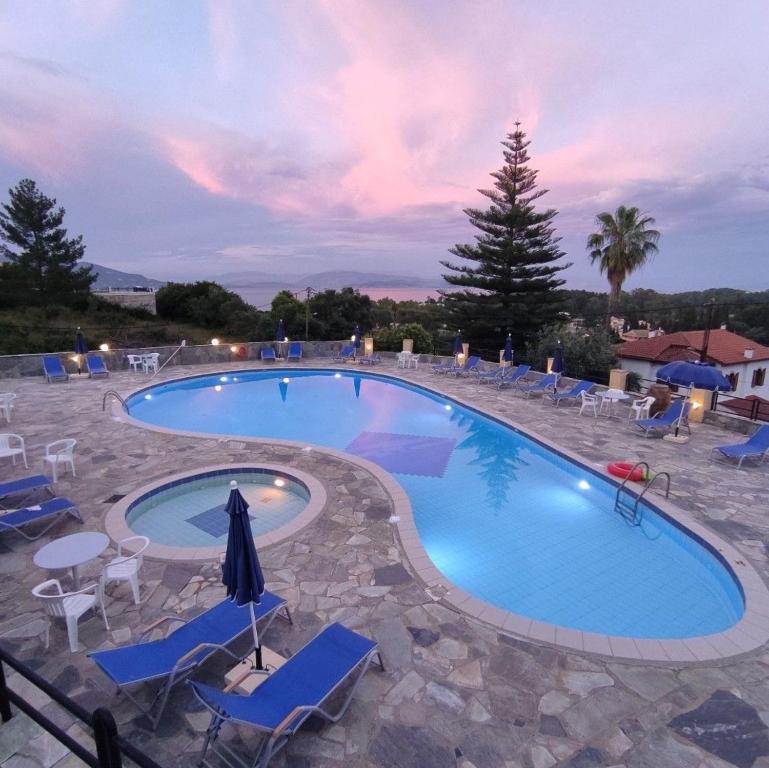 a large swimming pool with chairs and a sunset at Penelope Apartment Hotel in Dassia