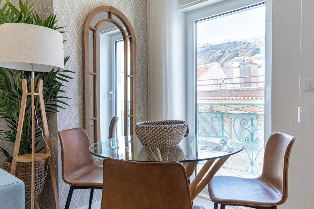 a dining room with a glass table and chairs and a window at Feel Nazaré - Saudade 57 in Nazaré