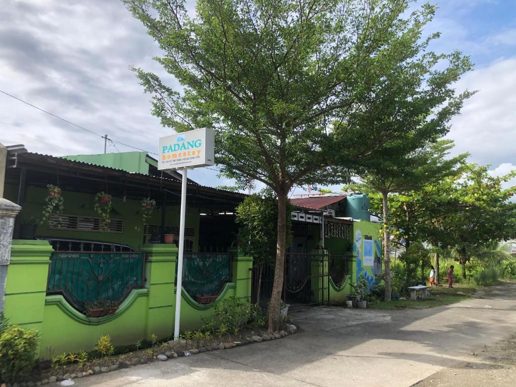 a green building with a sign in front of a tree at Padang Homestay in Padang