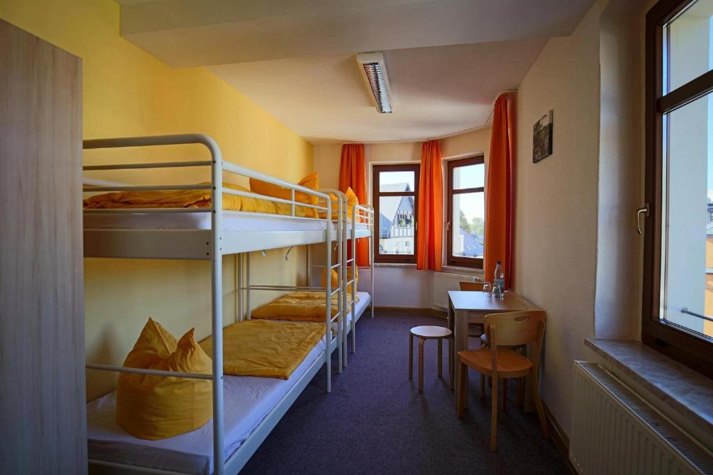 a room with bunk beds and a table and window at Wurzelrudis Hostel in Eibenstock