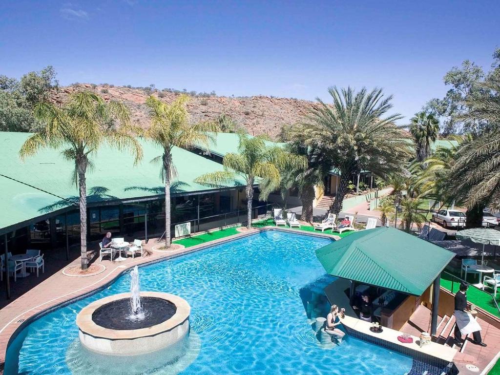 a large swimming pool with palm trees and a building at Mercure Alice Springs Resort in Alice Springs