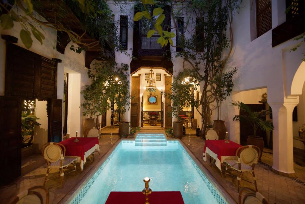 a large swimming pool in a building with tables and chairs at Riad Lyla in Marrakesh