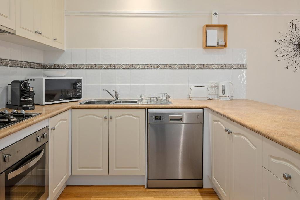 a kitchen with white cabinets and a stainless steel dishwasher at Yarra Gables in Healesville