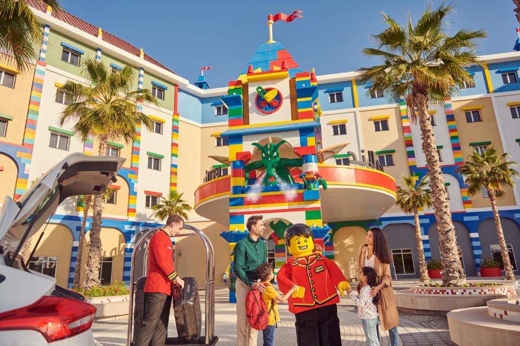 LEGOLAND Hotel Dubai في دبي: عائله تقف امام عماره فيها برج ساعه