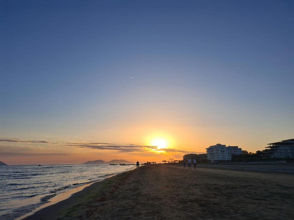 a sunset on the beach with people walking on the beach at Linda’s apartment in Vlorë