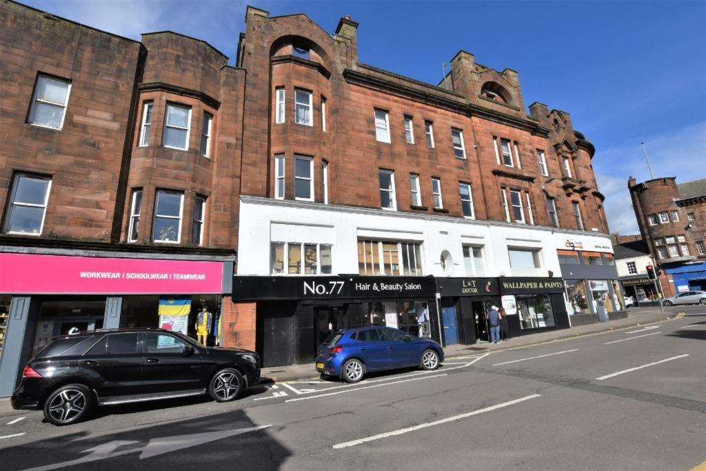 two cars parked in front of buildings on a city street at Dalblair Apartment in Ayr