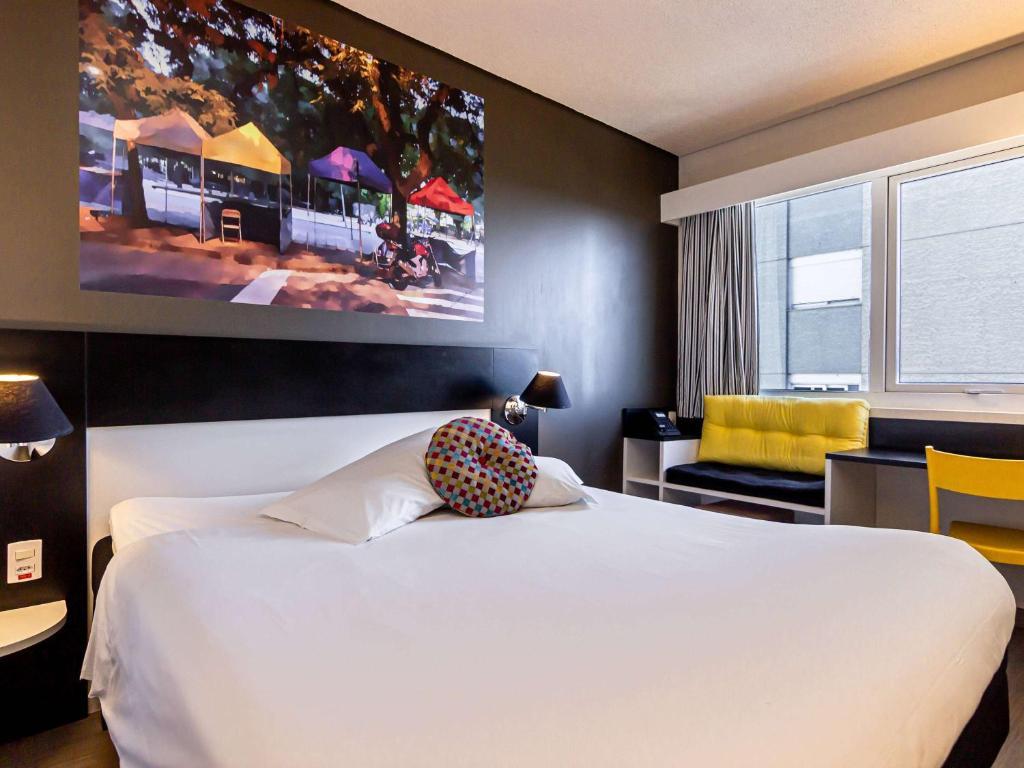 a bedroom with a white bed and a large painting on the wall at Ibis Styles Porto Alegre Centro in Porto Alegre