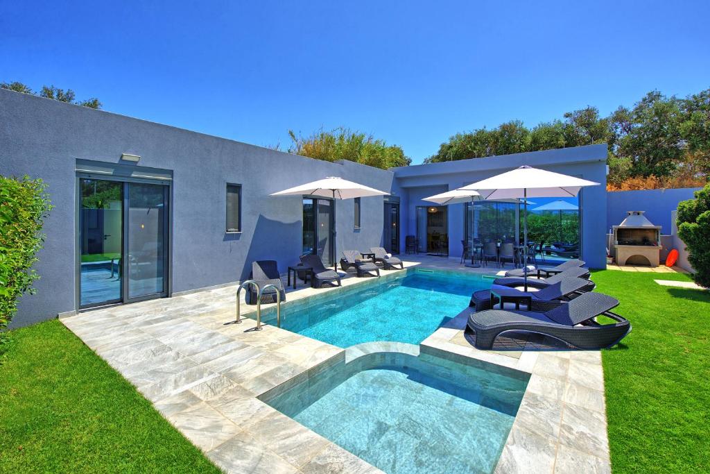 a backyard with a pool with chairs and umbrellas at Villa Zaneti by PosarelliVillas in Agia Marina Nea Kydonias