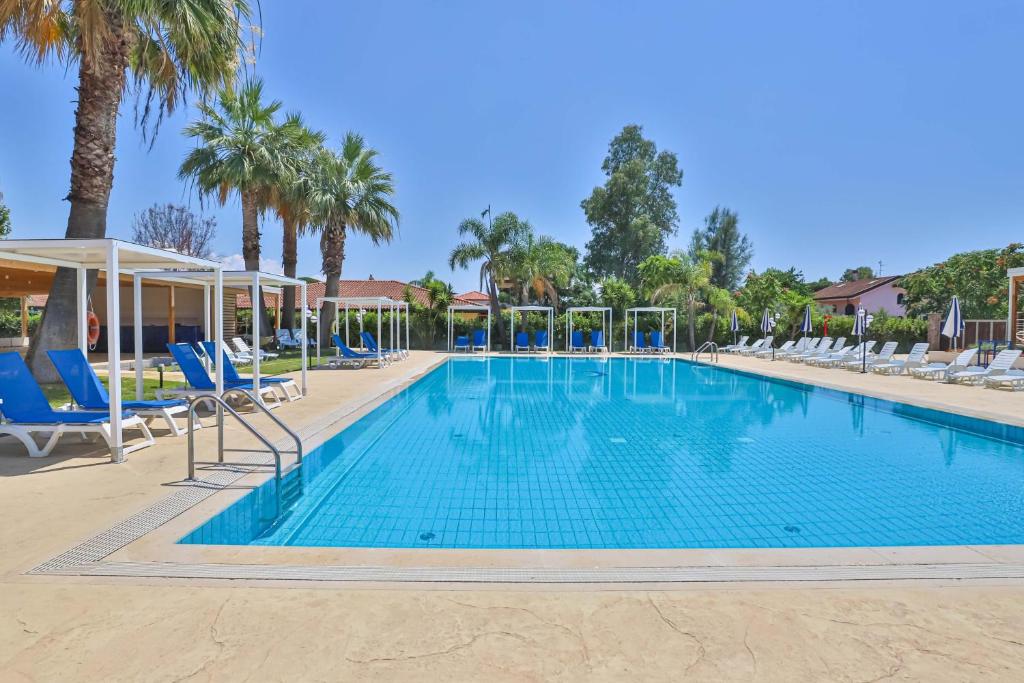 a large swimming pool with blue chairs and palm trees at Villaggio Selene Mare in Paestum