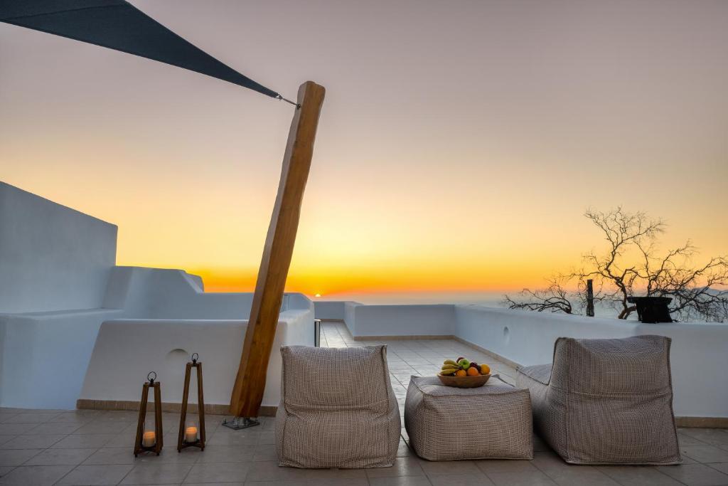 a patio with chairs and a sunset in the background at I K I A Since 1980 by Calm Collection in Fira