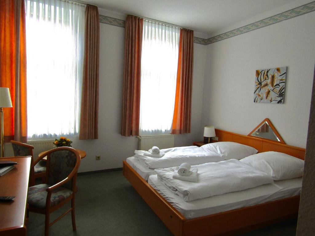 a bedroom with two beds and a chair and windows at Pension Hexenkessel in Wernigerode