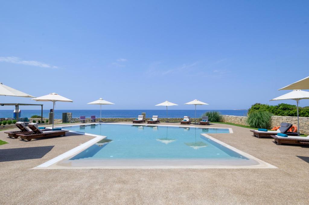 a swimming pool with chairs and umbrellas next to the ocean at Callisto Seaside Homes & Suites in Marathopoli