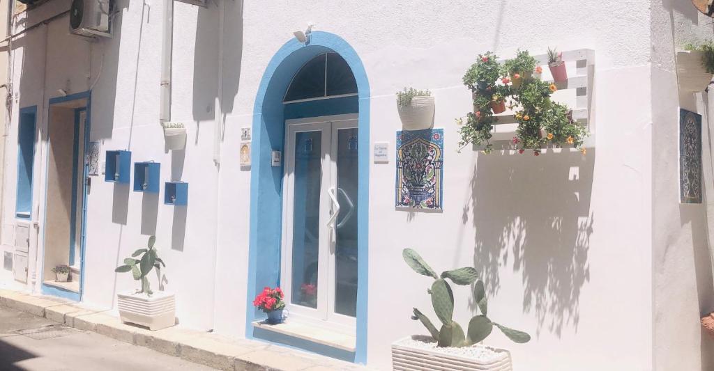 a white building with a blue door and potted plants at La Dimora del Viaggiatore Luxury Apartments in Mazara del Vallo