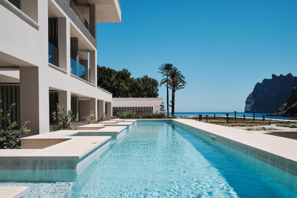 una piscina frente a un edificio con el océano en el fondo en El Vicenç de la Mar - Adults Only - Over 12 en Cala San Vicente