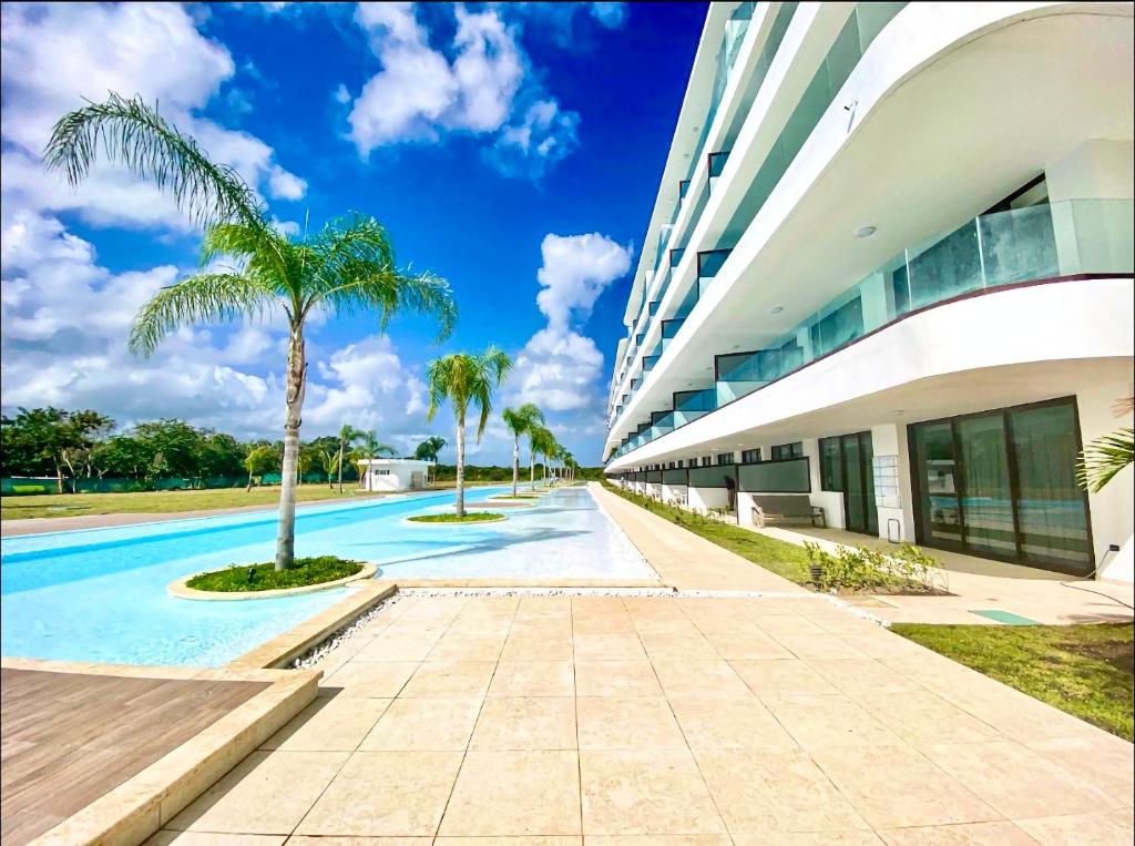 a building with a swimming pool next to a palm tree at Luxury Apartment With Pool And Golf View in Punta Cana