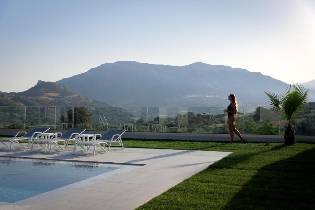 a woman walking by a pool with mountains in the background at Eolides Villas a mythical escape in Lambiní