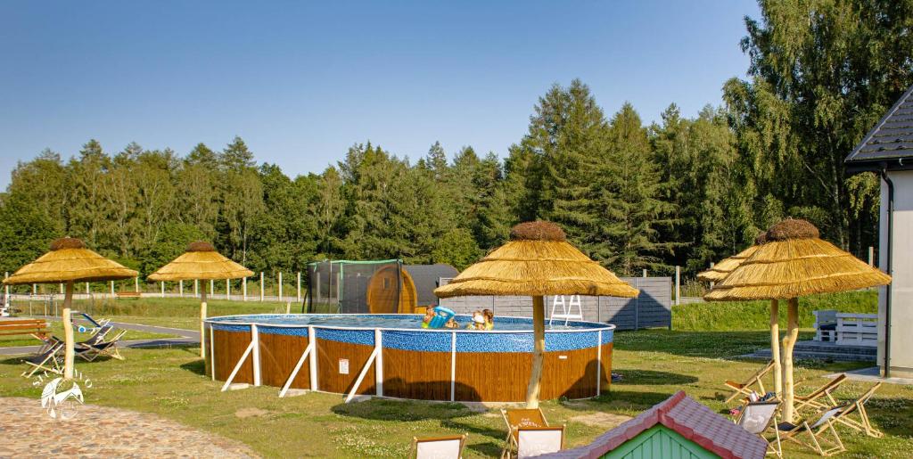 a pool with straw umbrellas in a park at Osada Słuszewo - Apartamenty Restauracja Wydarzenia in Gniewino