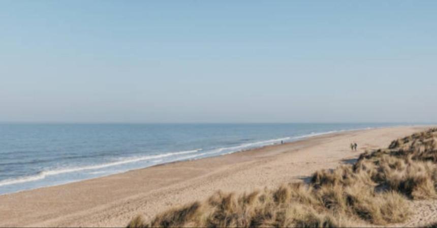 una spiaggia con persone che camminano sulla sabbia e sull'oceano di HemsbyholidaysRetroRetreat a Hemsby