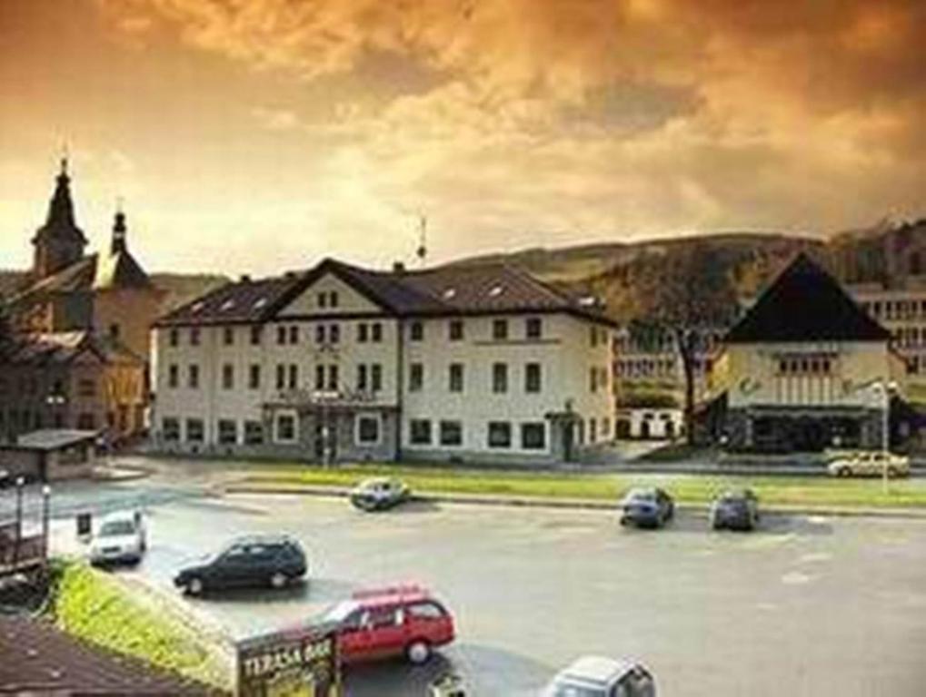 een groot wit gebouw met auto's geparkeerd op een parkeerplaats bij Hotel Krakonos in Rokytnice nad Jizerou