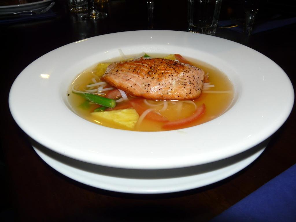 a white plate of food with a piece of fish in broth at Ski Time in Methven