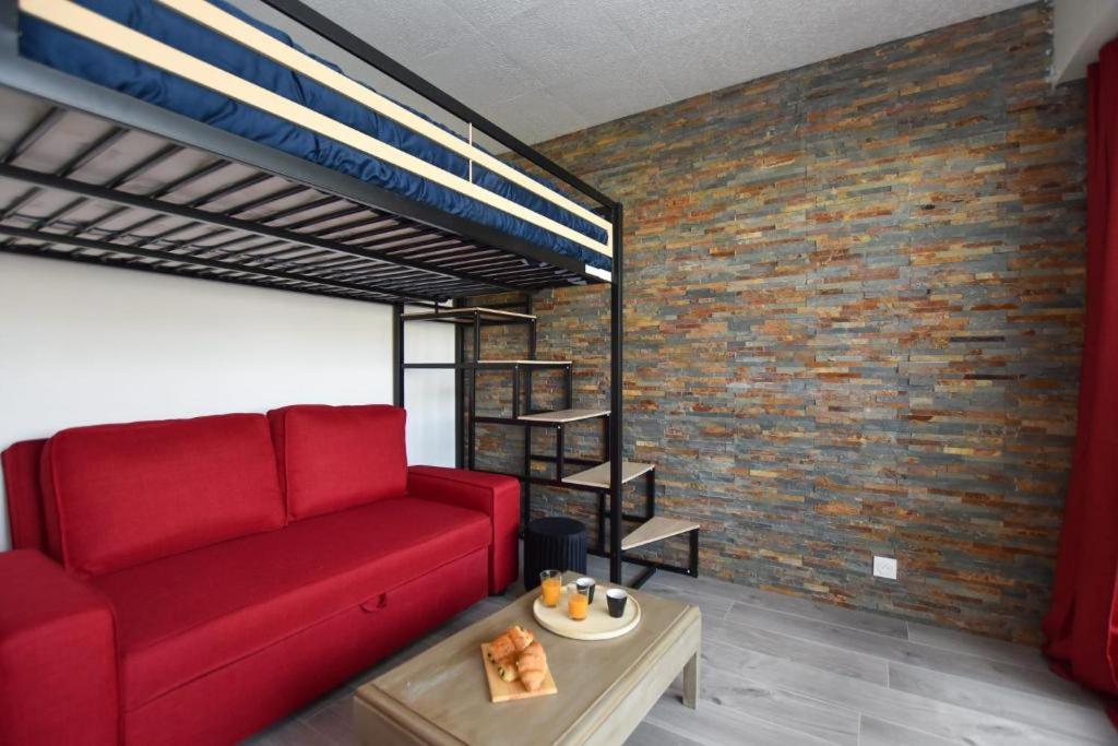 a living room with a red couch and a brick wall at Le P'tit bec ✹ Plage ✹ in Saint-Hilaire-de-Riez