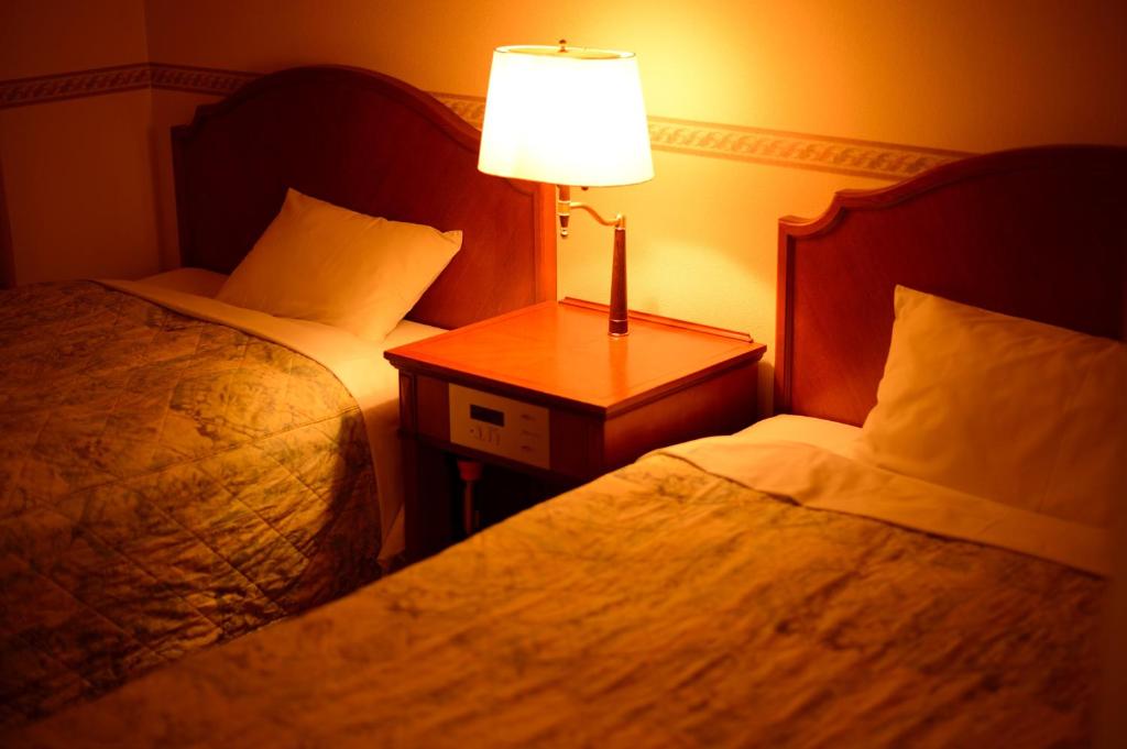 a hotel room with two beds and a table with a lamp at Hotel Bel Air Sendai in Sendai