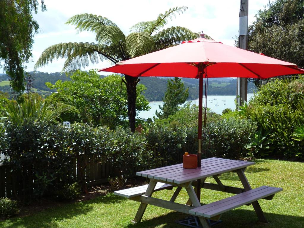 Opua Boutique Seaview Motel في Opua: طاولة نزهة مع مظلة حمراء ومقعد