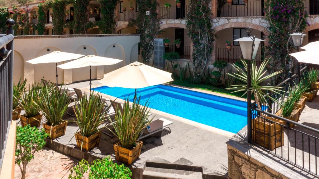 a swimming pool with umbrellas and plants next to a building at Hotel Abadia Plaza in Guanajuato