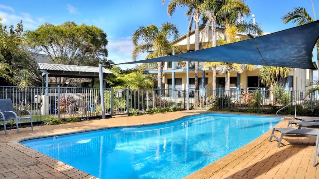 a swimming pool in front of a building with palm trees at Sorrento Apartments Merimbula in Merimbula