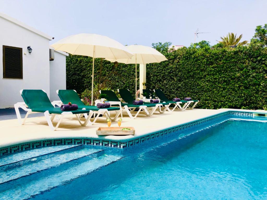 un grupo de sillas y sombrillas junto a una piscina en Villa Leon Menorca, tu casa menorquina!, en Cala'n Bosch