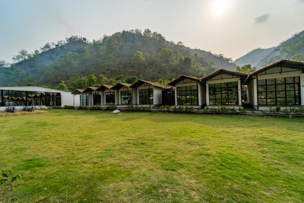 a row of buildings in a field with mountains in the background at The Ayali Riverside Resort in Rishīkesh