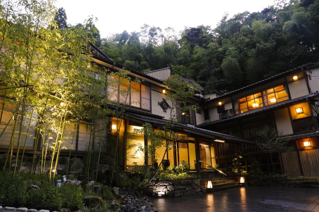 an asian house with lights on in a forest at Yuraku Kinosaki Spa & Gardens in Toyooka