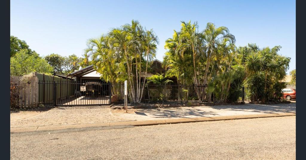 a fence in front of a house with palm trees at Kirei Pearl Accommodation Broome in Broome