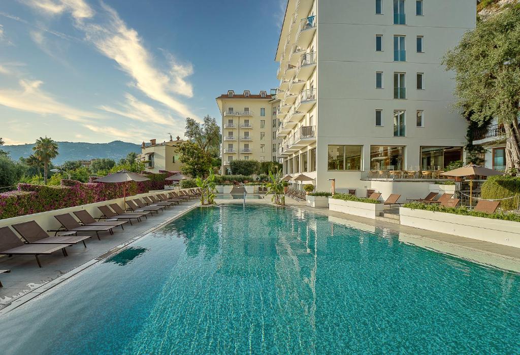 a large swimming pool with chairs and buildings at Hotel Conca Park in Sorrento