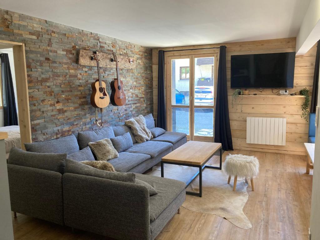 a living room with a couch and a guitar on a brick wall at Le très grand Appart in Uvernet