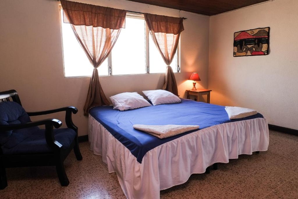 Un dormitorio con una cama y una silla y una ventana. en Hostal La Buena Onda, en Matagalpa