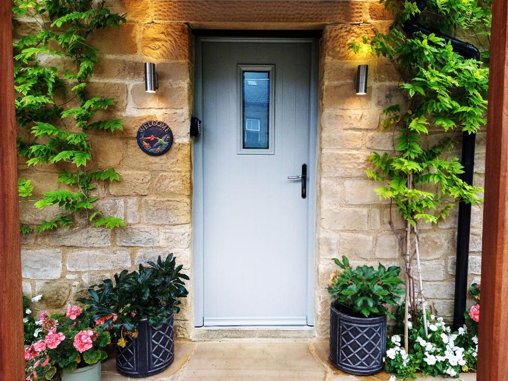 a white door on a stone house with two potted plants at The Nook Cottage In The Heart Of Northumberland in Wark